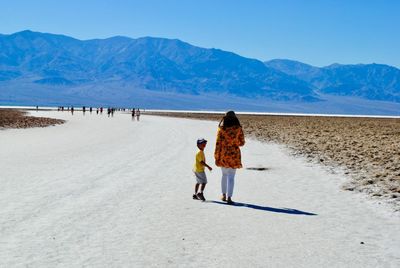 Portrait of boy with mother walking on dirt road against mountains