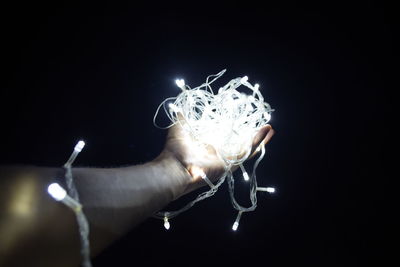 Close-up of hand holding illuminated lighting equipment against black background