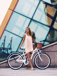 Portrait of young woman with bicycle standing against building