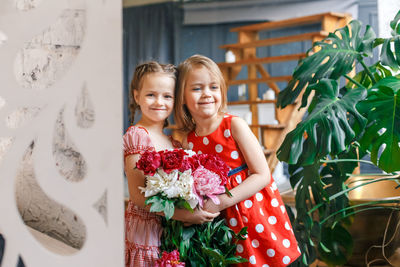 Portrait of cute smiling siblings with bouquet standing at home
