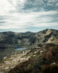 Scenic view of landscape against sky with a woman standing on a rock