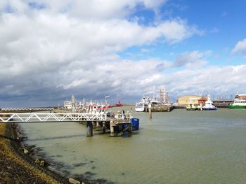 Boats in harbor against cloudy sky