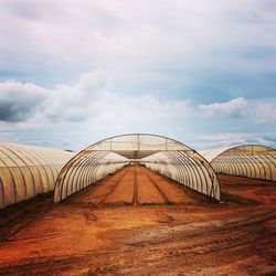 Empty greenhouses against cloudy sky