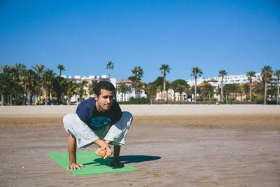 Full length of man doing yoga beach against clear blue sky