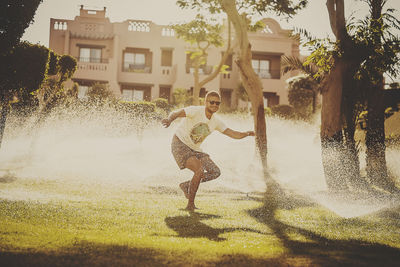 Playful man standing amidst sprinklers in yard