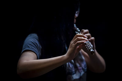 Close-up of person playing flute against black background