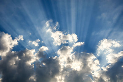 Low angle view of sunlight streaming through clouds