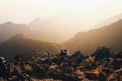 People sitting on mountain against sky during sunset