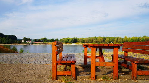 Chairs and table by lake against sky