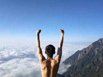 Rear view of shirtless man with arms raised against mountains