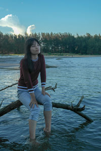 Young woman sitting by lake against sky