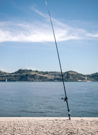 A fishing rod standing along the lisbon riverbank of tagus river near the belem tower.