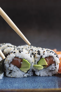 A set of fresh sushi rolls with salmon, avocado and sesame seeds with chopsticks