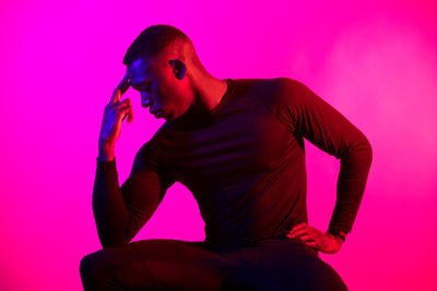 Young man sitting against pink background