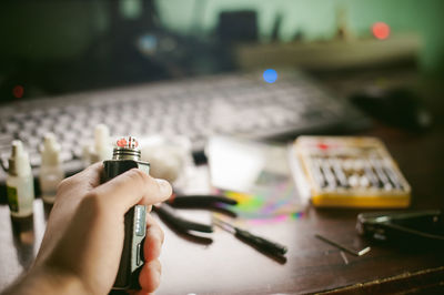 Close-up of hand holding electronic cigarette on table