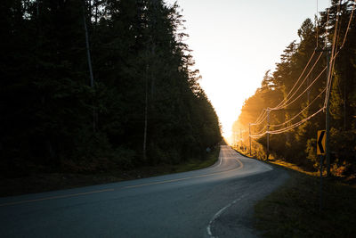 Empty road amidst trees against clear sky during sunset