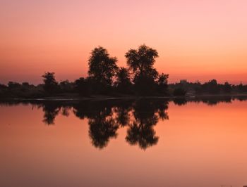 Reflection of silhouette trees in lake against orange sky