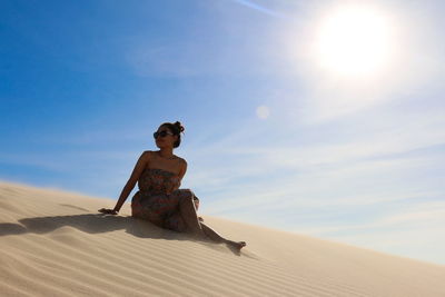 Woman sitting on sand dune in desert against sky