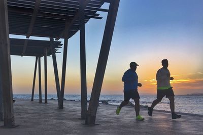 Men on beach against sky during sunset