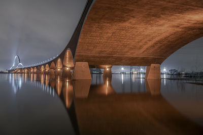 Illuminated bridge over river against sky at night and its reflection in the water