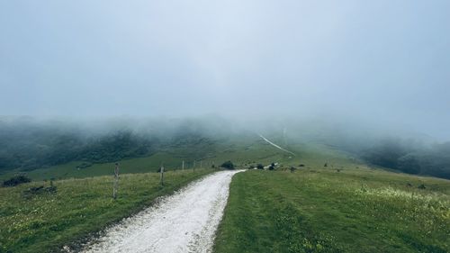Road amidst field against sky during foggy weather