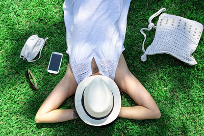 Young woman covered face with hat lying down on grass in field