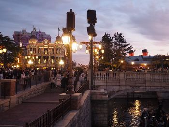 People on illuminated bridge over river in city at dusk