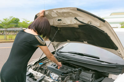 Rear view of woman checking car engine on road