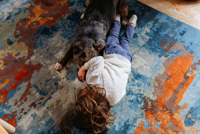 Upper view of child playing with dog on the carpet at home
