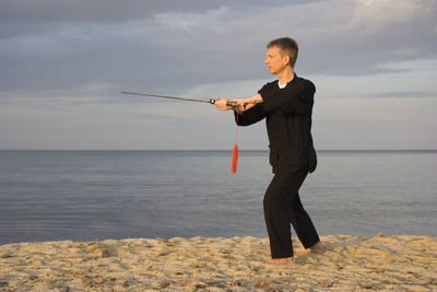 Man practicing tai chi at beach against cloudy sky