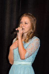 Young woman singing while standing against black curtain