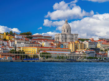 Buildings at waterfront against cloudy sky