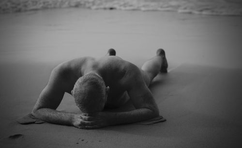 Rear view of shirtless man having sunbathing on beach