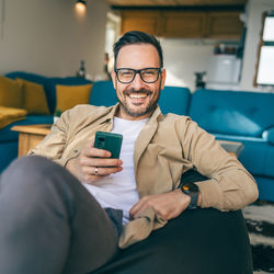 Young man using mobile phone while sitting on sofa at home