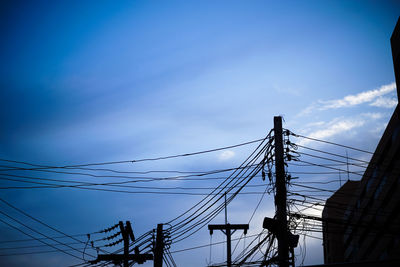 Low angle view of silhouette electricity pylon against blue sky