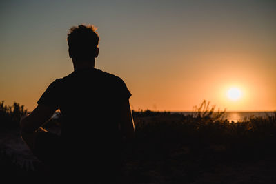 Rear view of silhouette man standing against orange sky