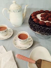 High angle view of tea cups with teapot by cake on table