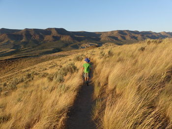 Rear view of boy walking on landscape against sky