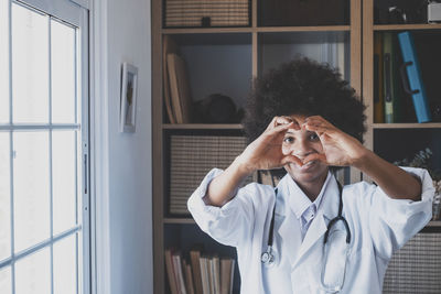 Portrait of young doctor making heart shape at clinic