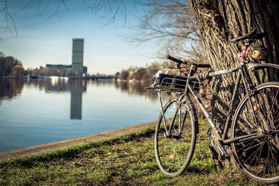 Bicycle parked by lake in city against sky