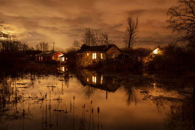 Houses by lake and buildings against sky during sunset