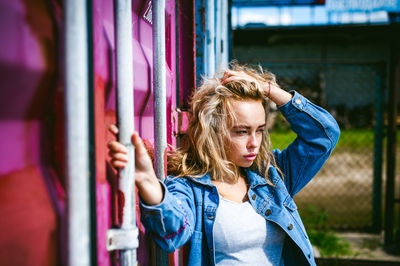 Young woman wearing denim jacket against metal structure