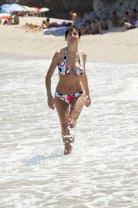 Seductive woman wearing bikini wading in sea during sunny day