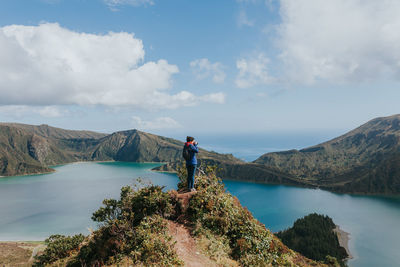 Man standing on rock by lake against sky