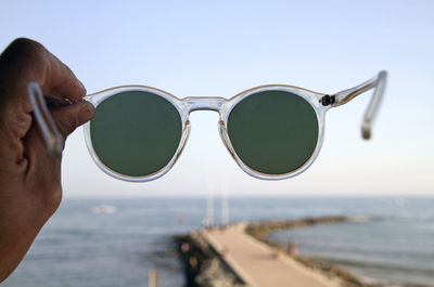 Midsection of woman holding sunglasses at beach against sky
