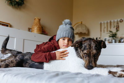 Gilr wearing grey warm hat hug her dog which is wearing sweater