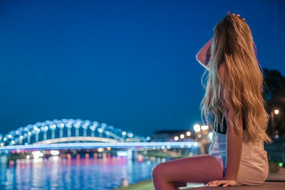 Rear view of woman sitting against river at night