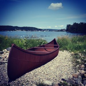 Boat moored on shore by lake against sky