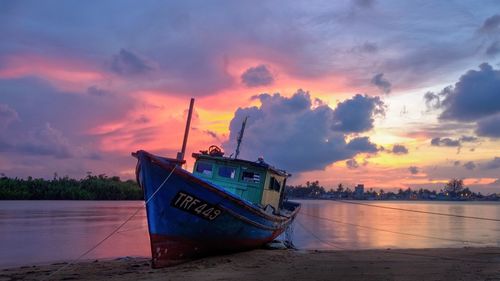 Boat moored at beach against sky during sunset