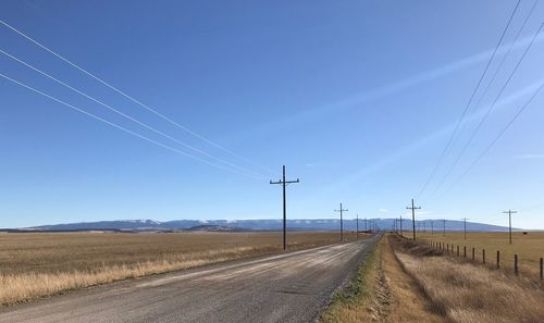 Road by electricity pylon against blue sky